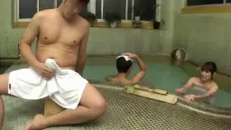 Nackter Mann mit weißem Handtuch sitzt am Onsen-Beckenrand, während eine Japanerin im Hintergrund im heißen Wasser liegt.