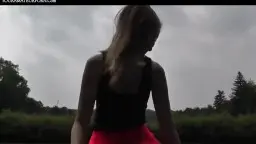 Blonde Oma in rotem Rock reitet ihren Enkel auf einer Wiese unter grauem Himmel.