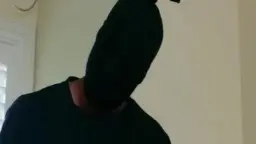Maskierter Mann in schwarzem Shirt steht in hellem Schlafzimmer und blickt auf Scarlet Young herab