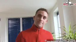 Junger Mann im roten Rolli lächelt selbstbewusst in die Kamera, helles Wohnzimmer im Hintergrund
