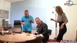 Blonde Chefin mit Brille und gestreiftem Kleid steht dominant im Büro und beobachtet ihre Kollegen am Besprechungstisch