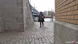 Schwarzhaarige Frau in dunkelgrüner Bluse und offenem Mantel läuft lächelnd durch eine urbane Gasse.