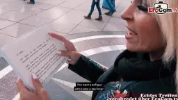 Blonde Milf mit weißem Haar hält lächelnd ein Schild in der Fußgängerzone