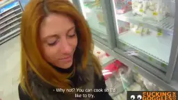 Rote Schönheit mit langen Haaren steht verführerisch lächelnd im Supermarkt vor der Kühltheke.