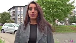 Reife Dunkelhaarige mit Lederjacke blickt verführerisch in die Kamera vor Hochhaus-Siedlung