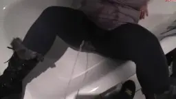 Rothaarige Tante in Leggings und Stiefeln sitzt breitbeinig auf dem Toilettenrand und pisst einen starken Strahl in die Kloschüssel.