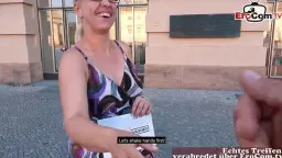 Geile blonde MILF mit Brille kniet nackt vor muskulösem Mann und saugt tief an seinem Schwanz.