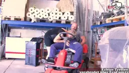 Blonde MILF kniet in schwarzem Kleid zwischen den Beinen ihres Chefs im Lagerhaus und saugt hingebungsvoll an seinem harten Schwanz