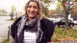 Lächelnde blonde Milf mit Locken und Schal steht draußen vor einem Gebäude
